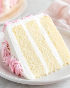 Slice of moist vanilla cake with pink frosting decoration on a white plate
