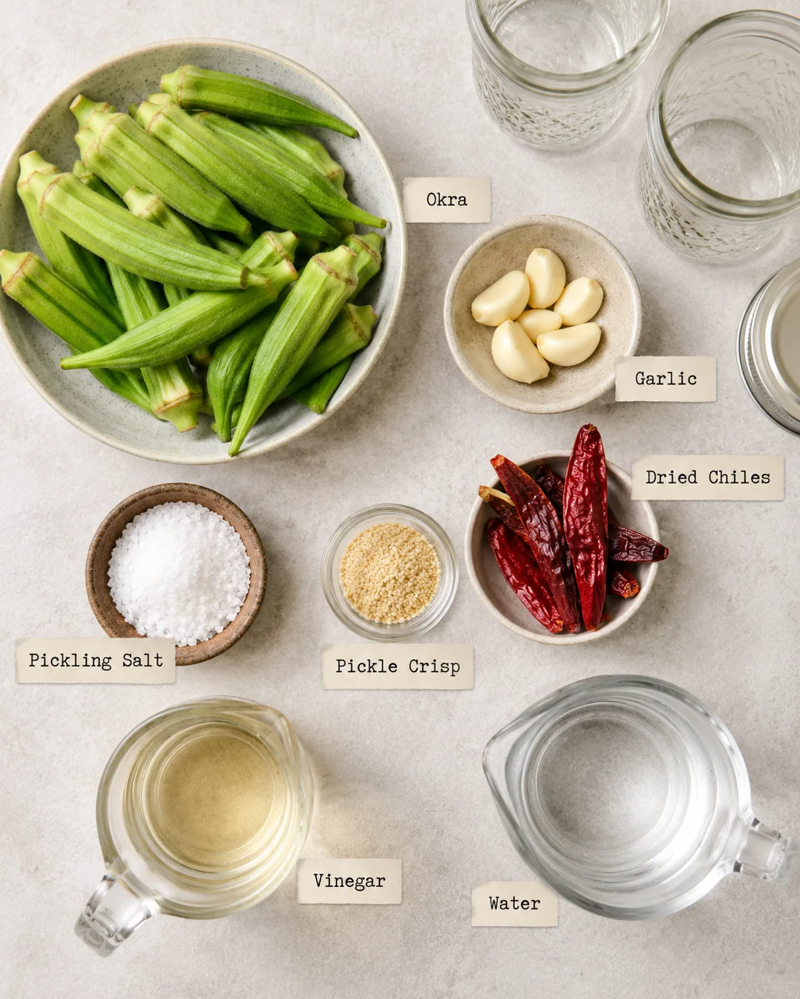 Fresh green okra, garlic, dried chiles, and pickling ingredients arranged on a table.