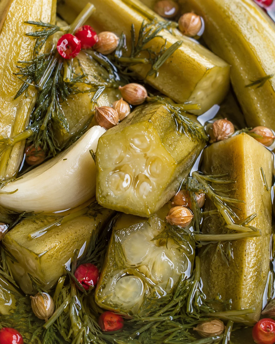 Close-up of fresh pickled okra with garlic, dill, and red peppercorns in brine.