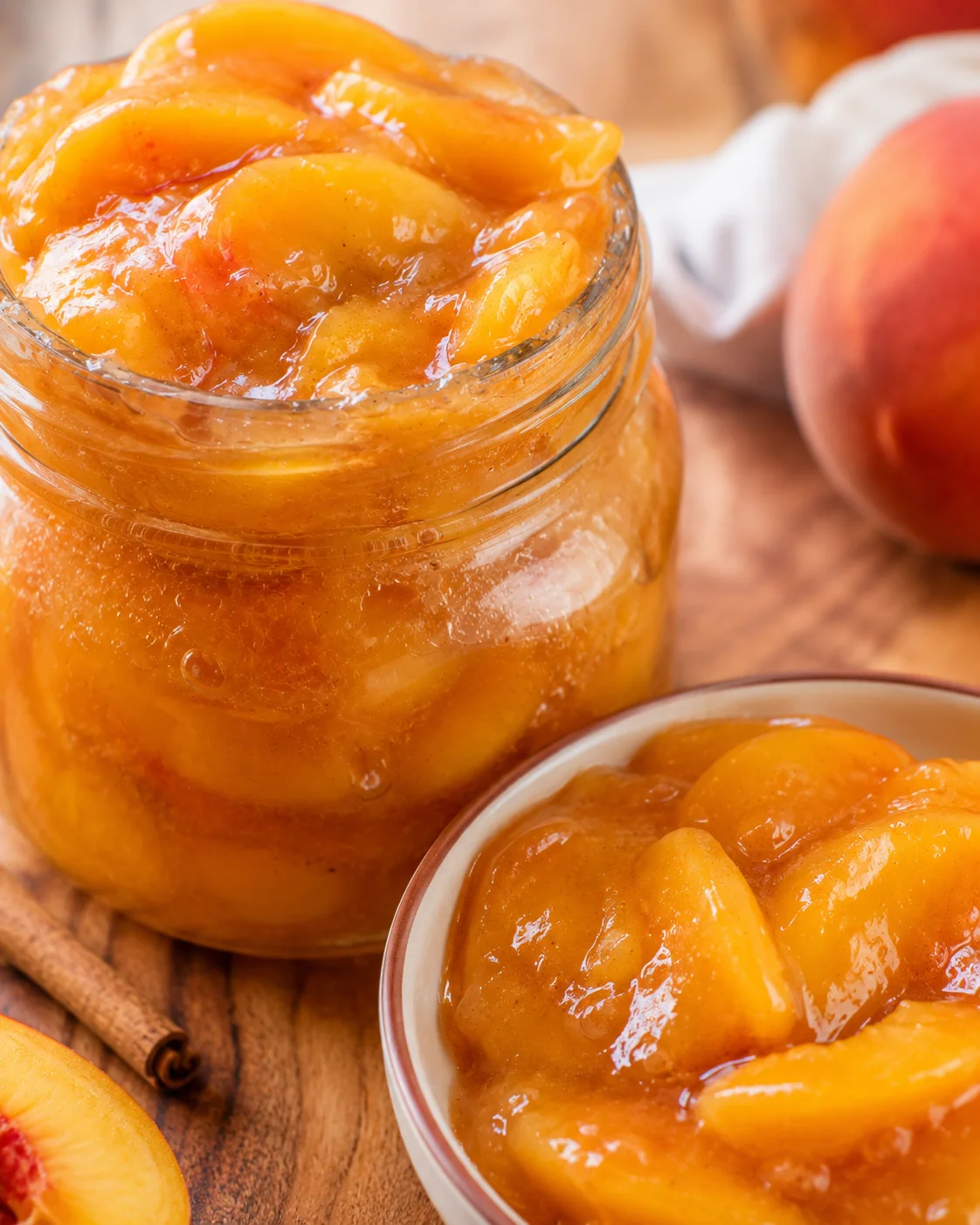Jar of homemade canned peach pie filling with fresh peaches nearby