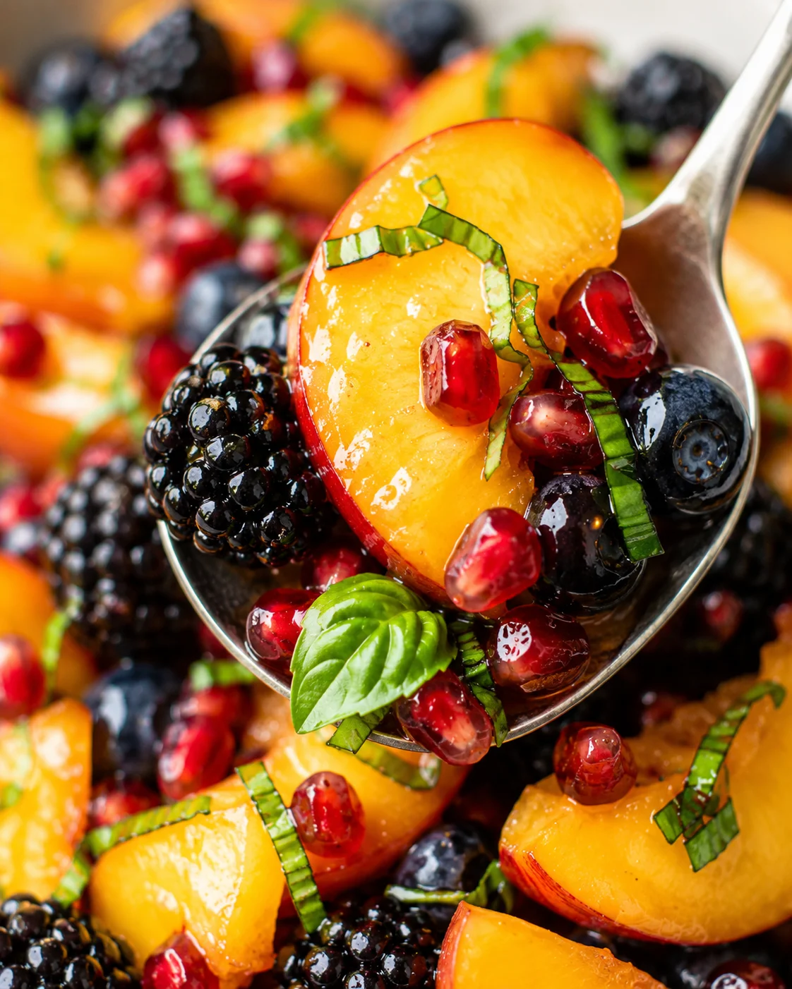 Close-up of fresh peach fruit salad with berries and basil on a spoon