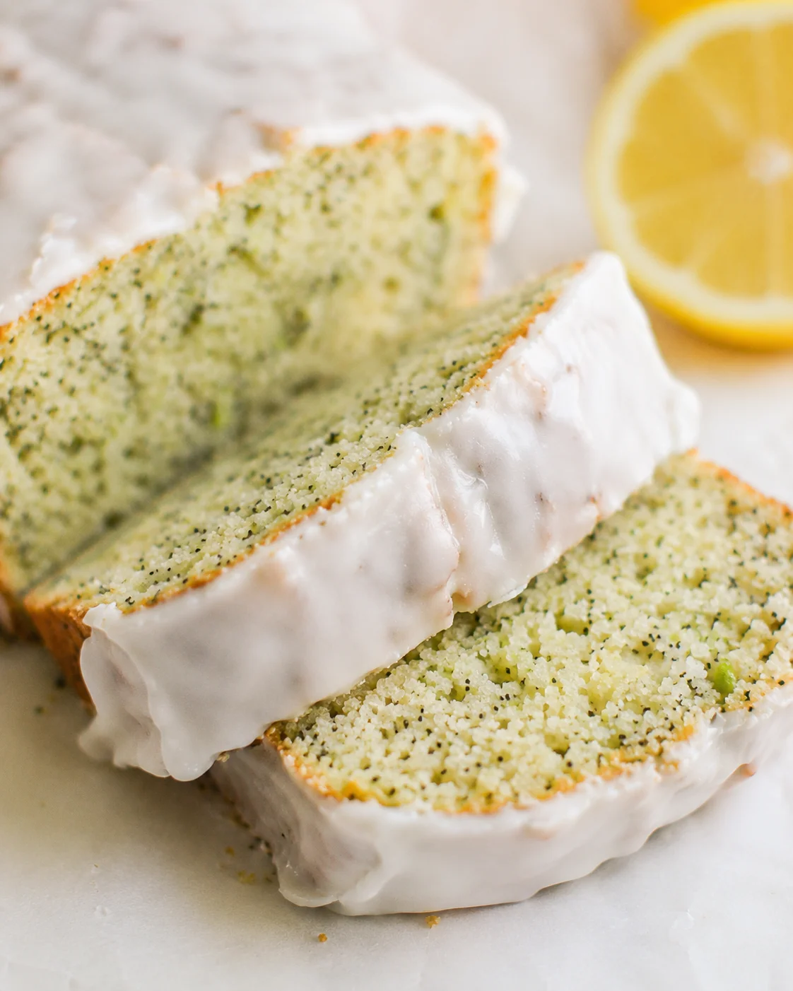 Close-up of lemon zucchini bread slices with white glaze and lemon slices in background