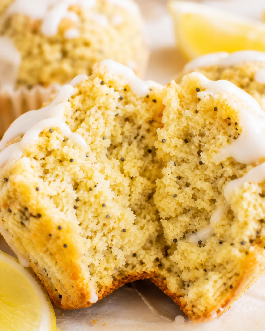 Close-up of a moist lemon poppy seed muffin with lemon slices in the background.