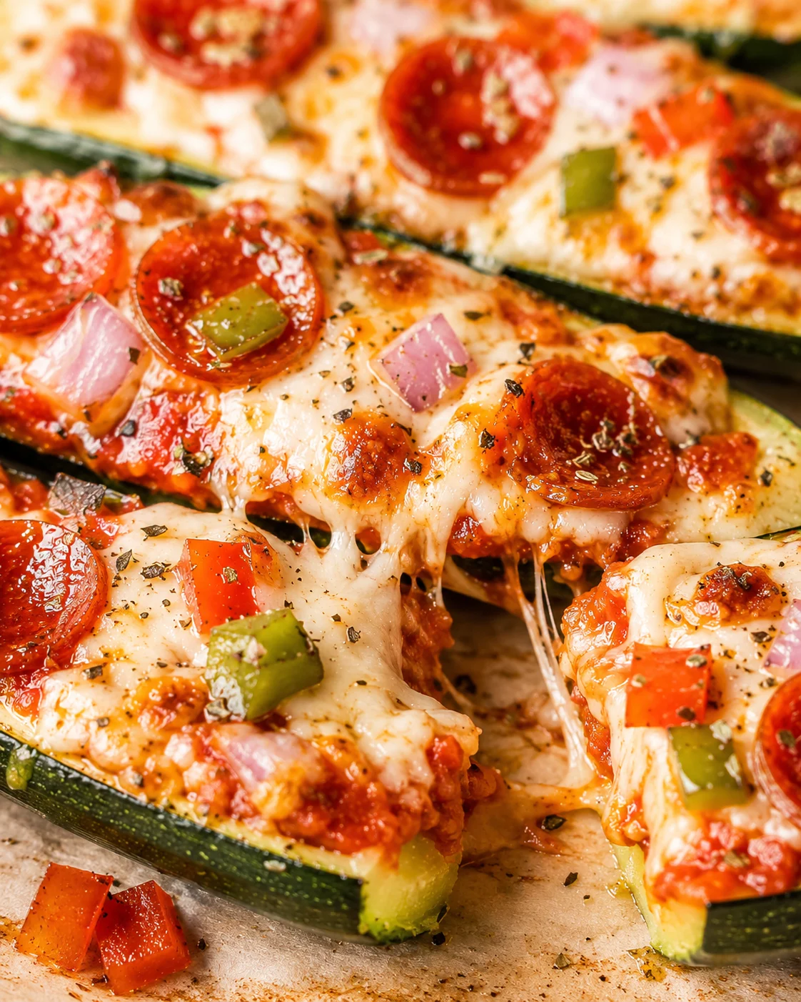 Close-up of cheesy zucchini pizza boats topped with pepperoni and vegetables.