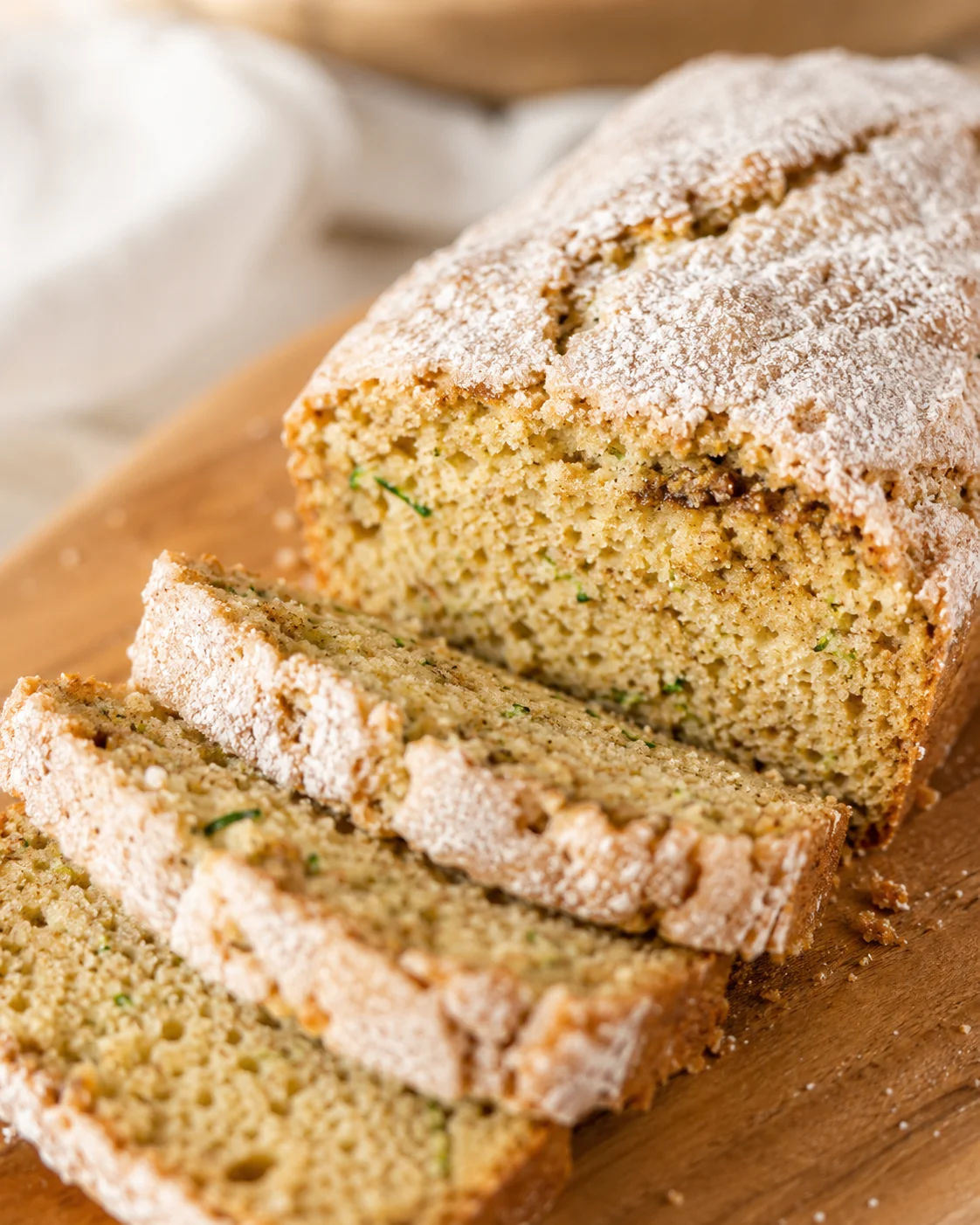 Close-up of sliced snickerdoodle zucchini bread dusted with powdered sugar on a wooden cutting board.