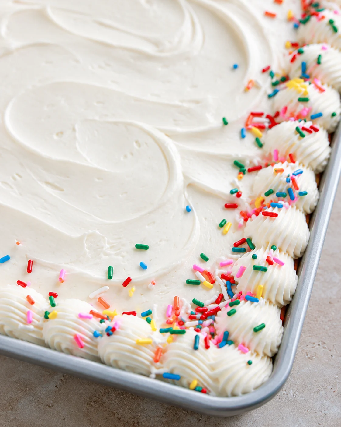 Delicious vanilla sheet cake decorated with colorful rainbow sprinkles and whipped frosting