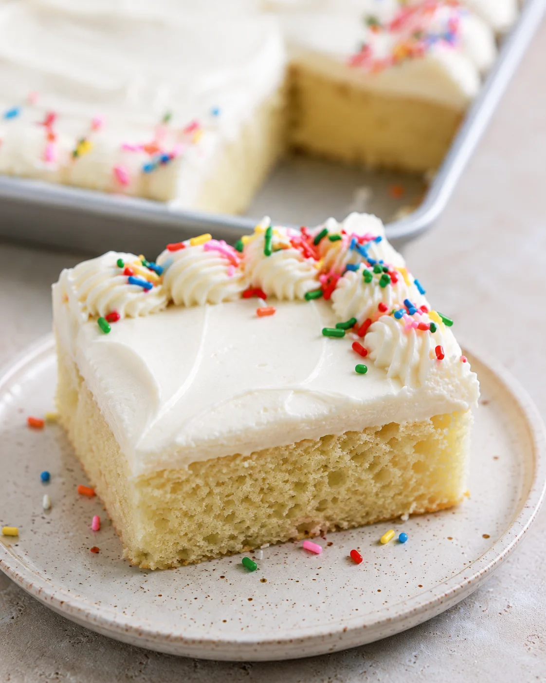 Moist vanilla sheet cake topped with white frosting and colorful rainbow sprinkles.
