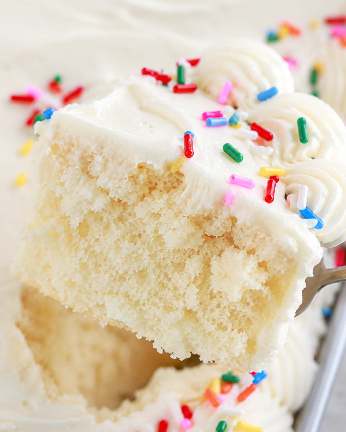 Close-up of a moist vanilla sheet cake with colorful sprinkles and creamy frosting