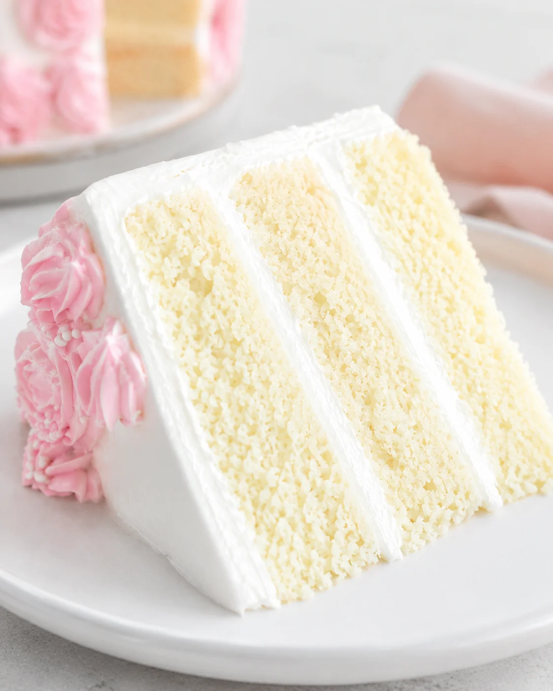 Slice of moist vanilla cake with white frosting and pink decorations