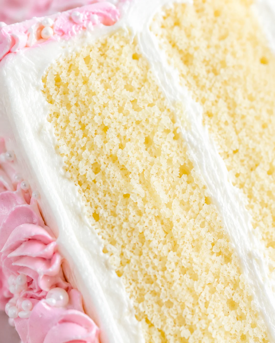 Close-up of a slice of moist vanilla cake with tender crumb and pink frosting