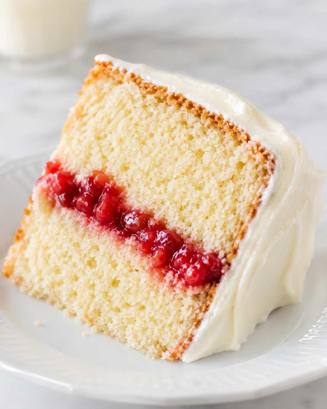 Slice of vanilla cake with strawberry filling and cream cheese frosting on a plate