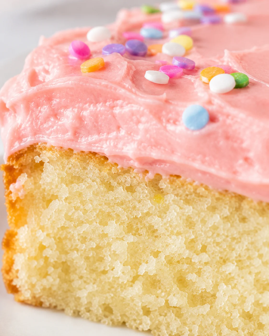 Close-up of a mini vanilla cake with pink frosting and colorful sprinkles