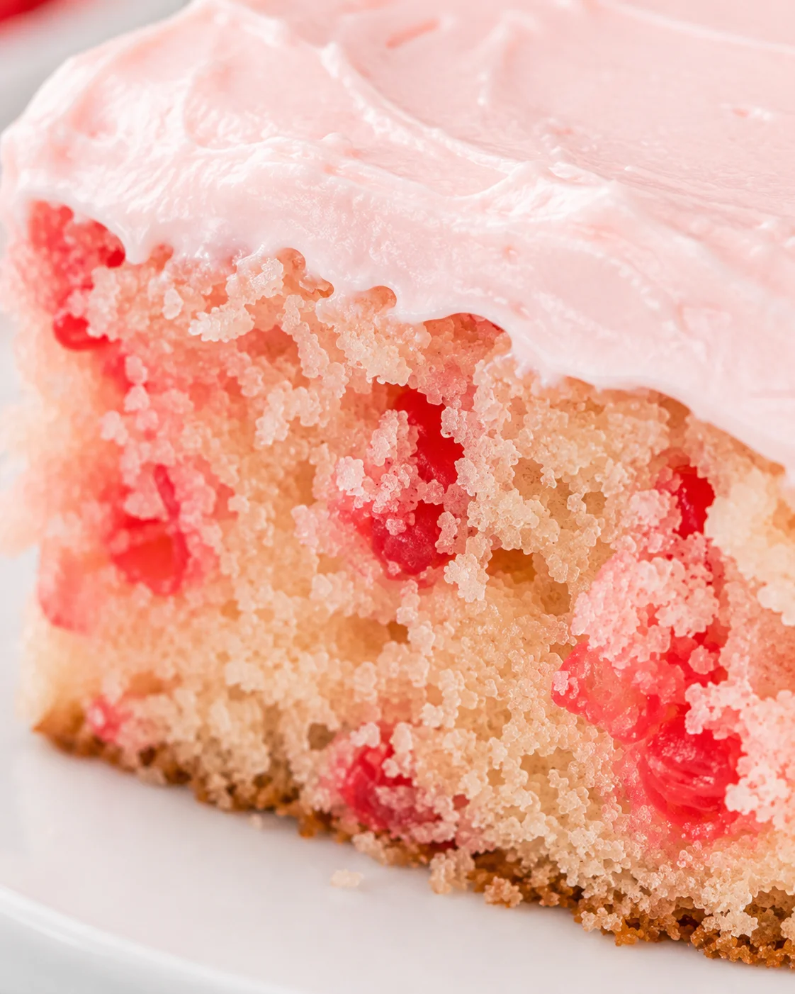 Close-up of a moist cherry vanilla cake slice with pink frosting and cherry pieces.