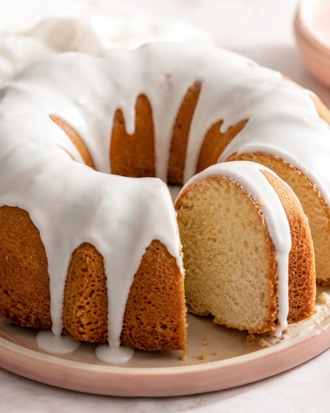 Moist vanilla bundt cake topped with a glossy white glaze on a plate.