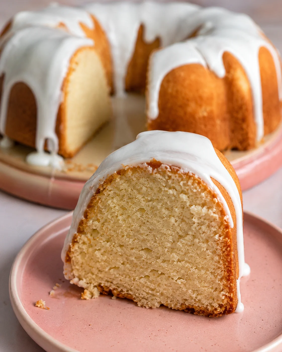 A sliced vanilla bundt cake topped with a glossy white glaze on a pink plate
