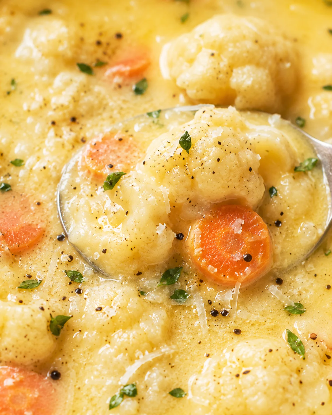 Close-up of creamy cauliflower and carrot soup garnished with herbs and black pepper.