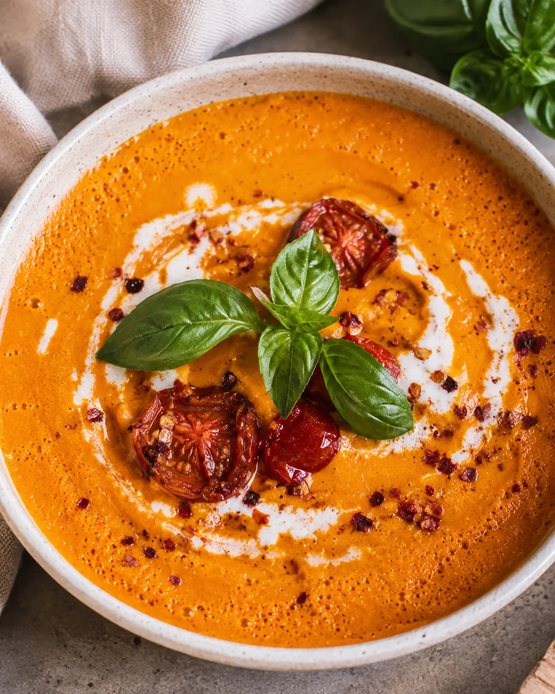 A bowl of creamy roasted tomato carrot soup garnished with basil and sun-dried tomatoes.