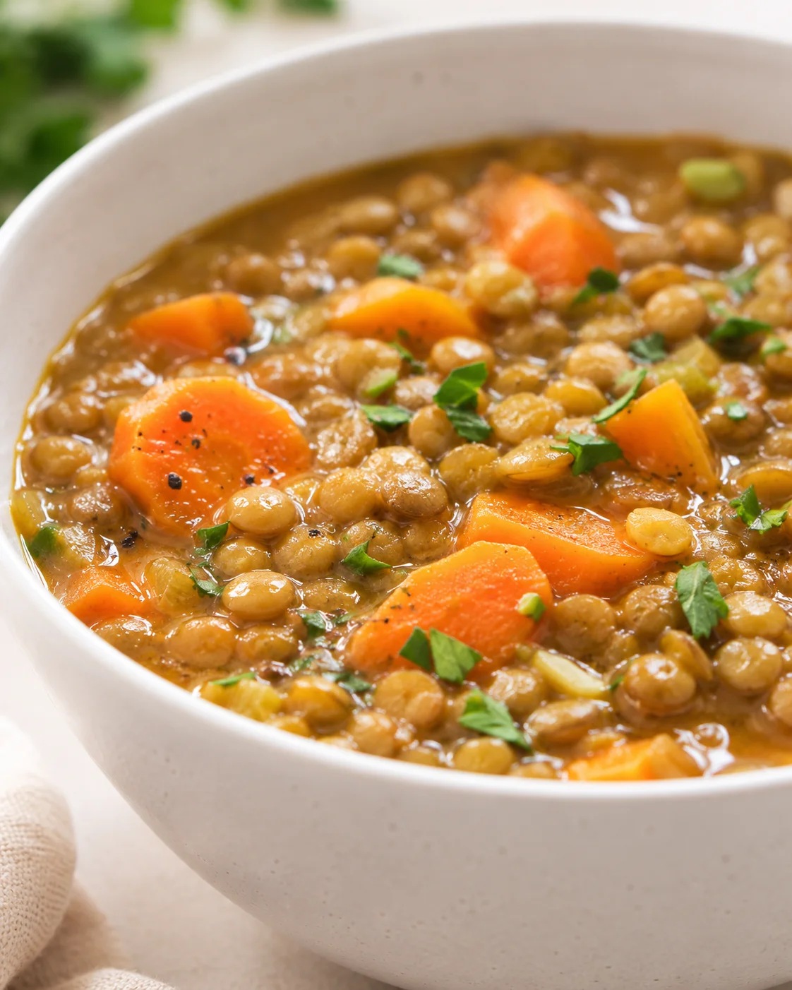 A bowl of warm carrot and lentil soup garnished with herbs and pepper.