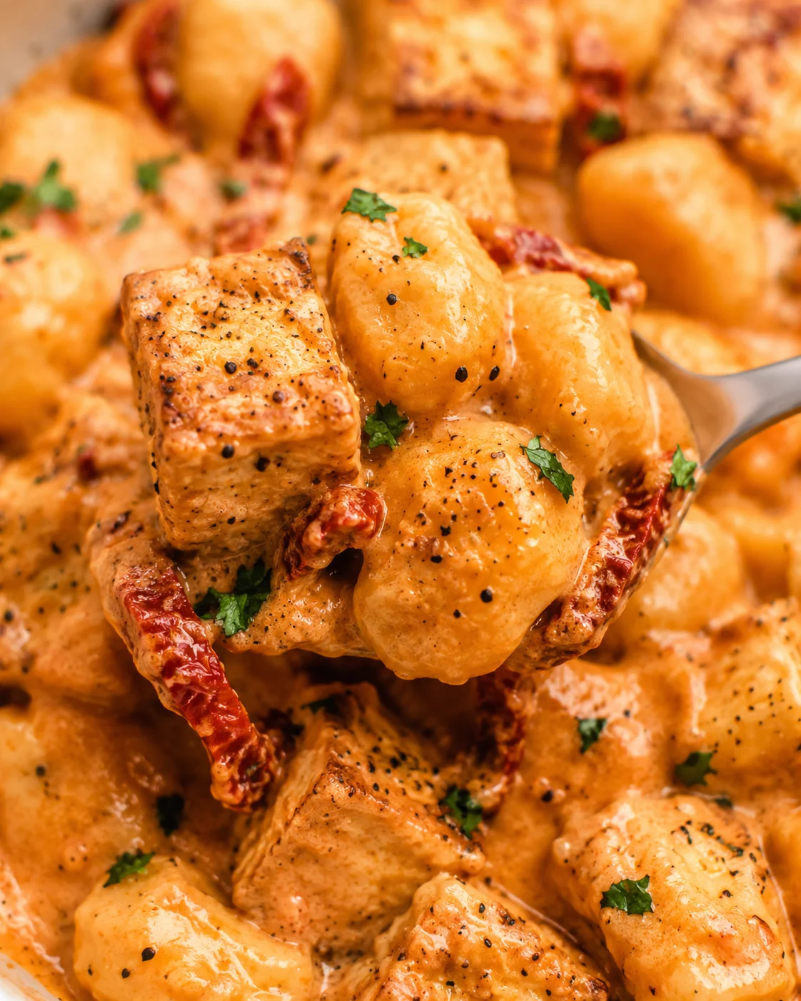 Close-up of crispy tofu cubes in a rich, tomato sauce with gnocchi garnished with herbs