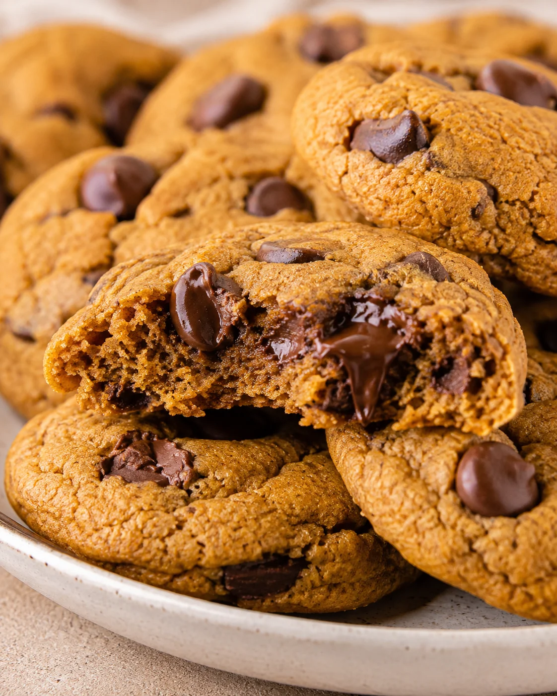 Plate of chewy pumpkin chocolate chip cookies with one cookie partially bitten to show melted chocolate
