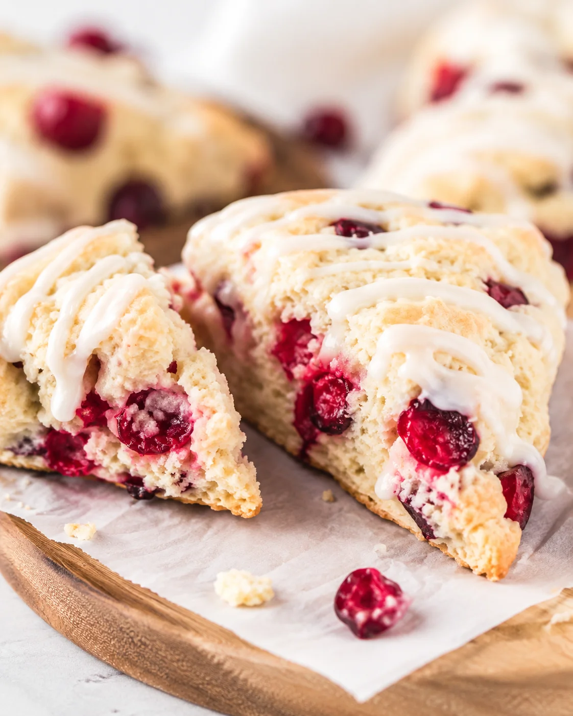 Two cranberry scone wedges with glaze on a parchment-lined wooden board