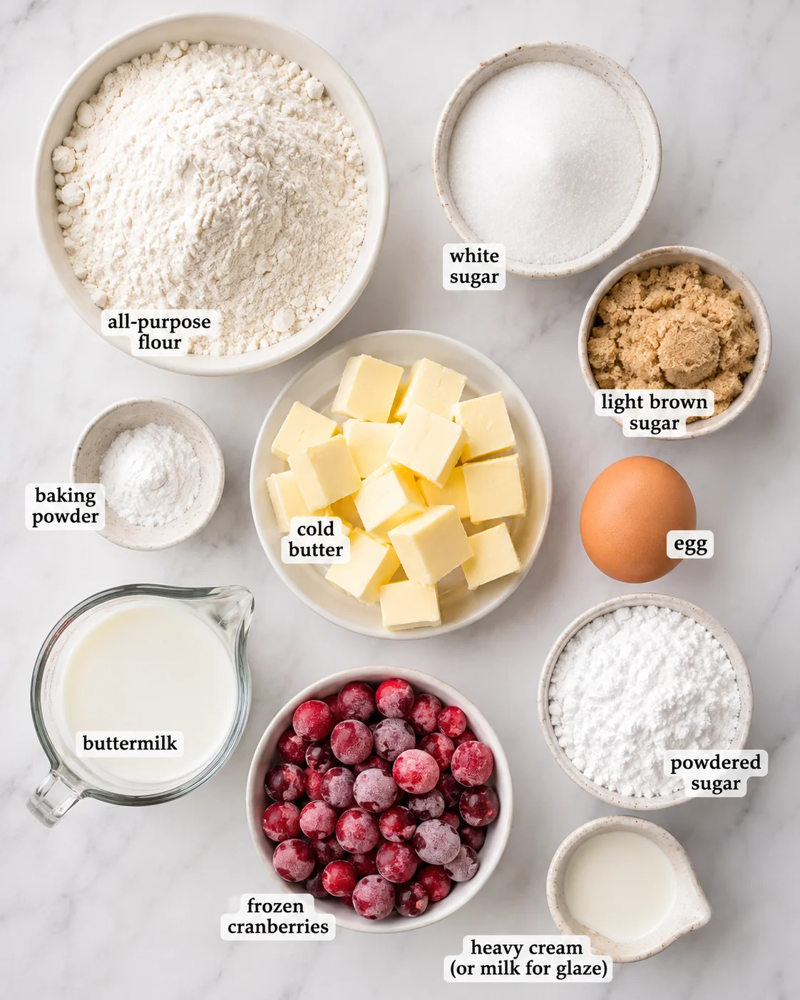 Top-down arrangement of measured ingredients for cranberry scones including flour, butter, sugars, buttermilk and frozen cranberries