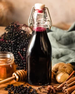 Swing-top bottle of elderberry syrup on a wooden board with honey, ginger and spices