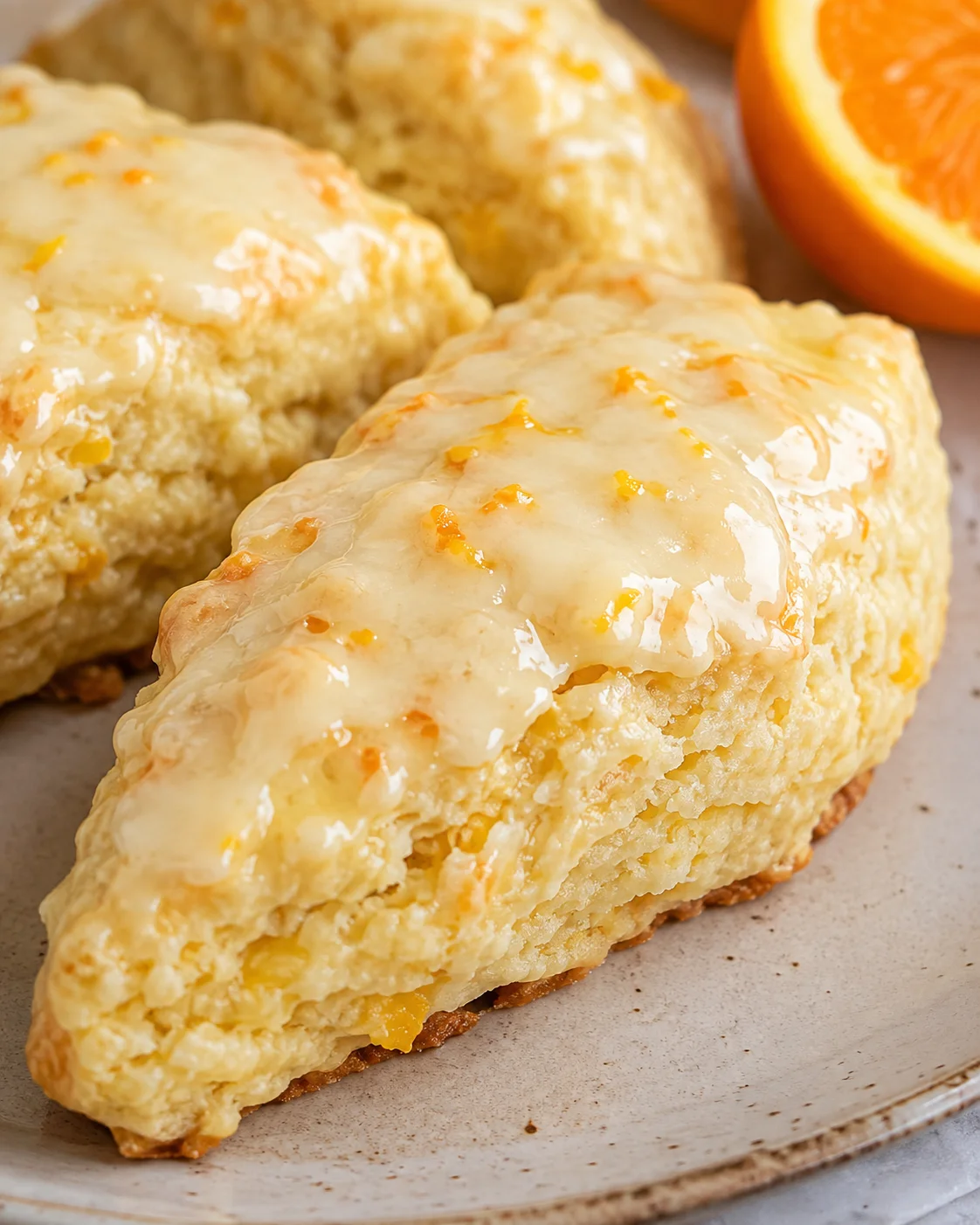 Close-up of a single glazed orange scone showing orange zest and glaze