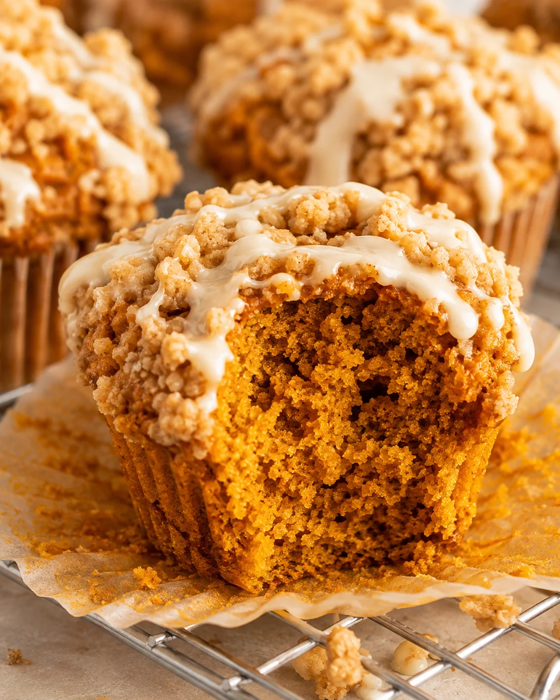 Close-up of a gluten free pumpkin muffin with streusel topping and maple glaze, interior and wrapper visible