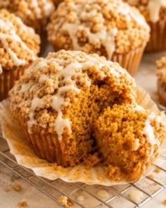 Gluten free pumpkin muffin with a piece removed, topped with streusel and maple glaze on a cooling rack