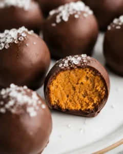 Plate of healthy pumpkin truffles with one truffle cut to show the pumpkin filling and flaky sea salt on top