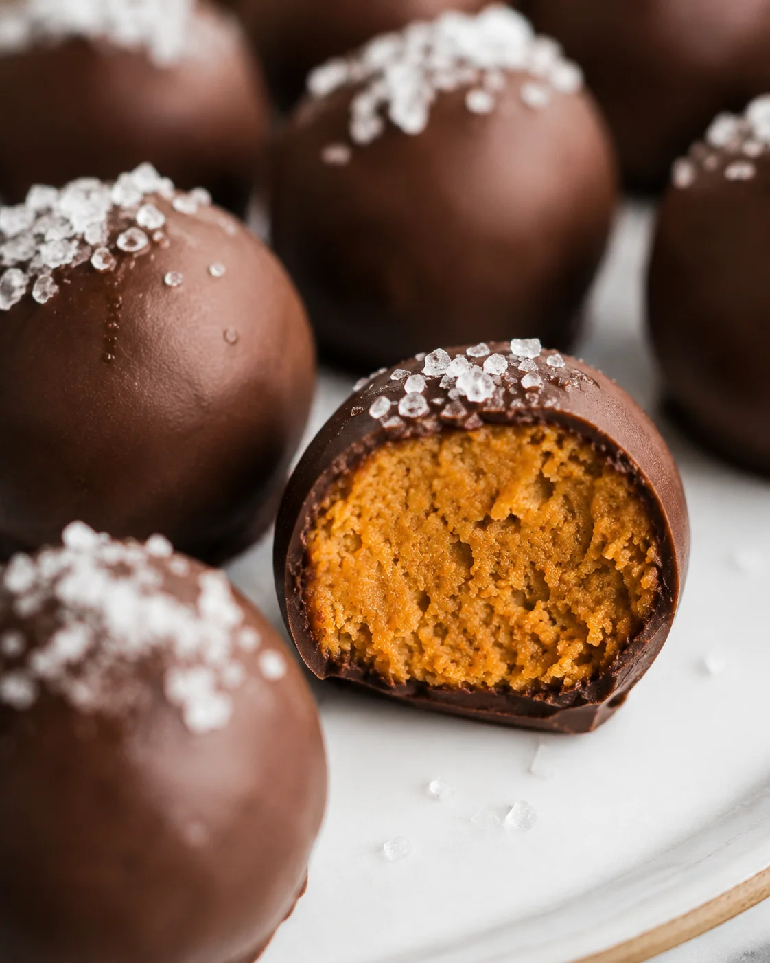 Plate of healthy pumpkin truffles with one truffle cut to show the pumpkin filling and flaky sea salt on top