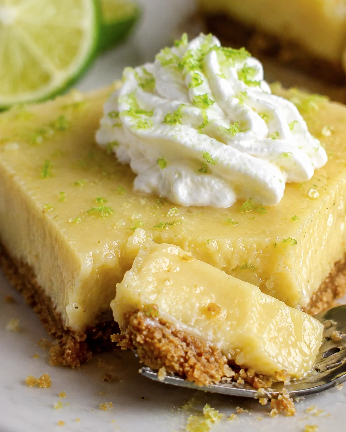 Fork cutting into a key lime pie bar showing creamy filling and graham crust beneath whipped cream