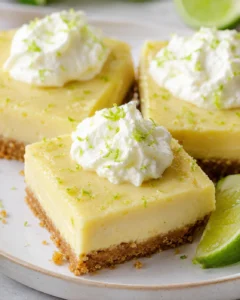 Three key lime pie bars on a plate topped with whipped cream and lime zest