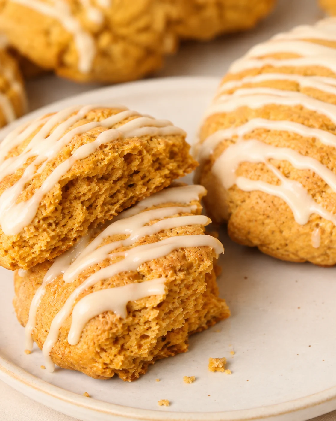 Plate with two maple pumpkin scones, one split to show the tender interior, drizzled with maple glaze.