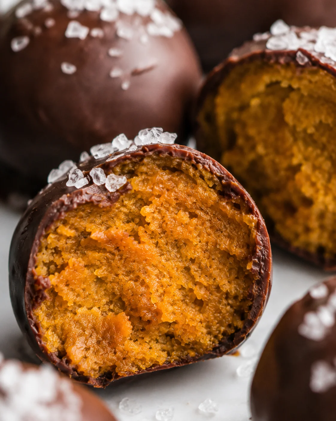 Macro detail of the pumpkin truffle interior showing moist orange filling and chocolate edge with sea salt