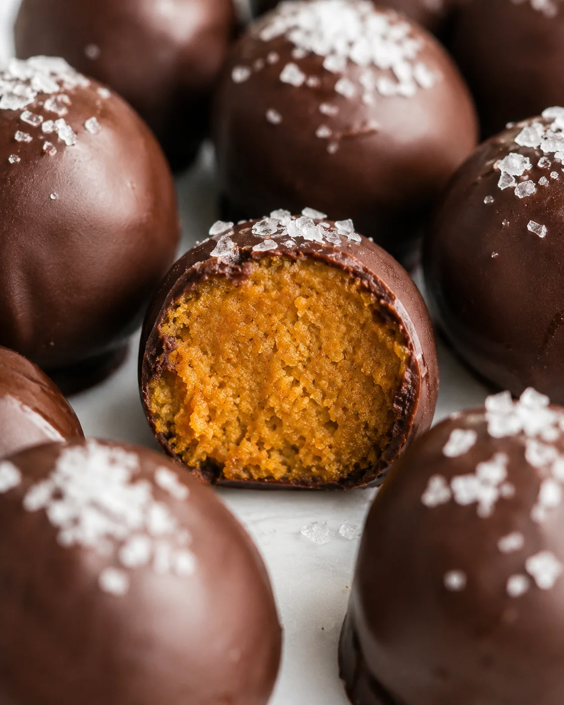Close side view of chocolate-coated pumpkin truffles with a bitten truffle showing the pumpkin interior and flaky sea salt on top