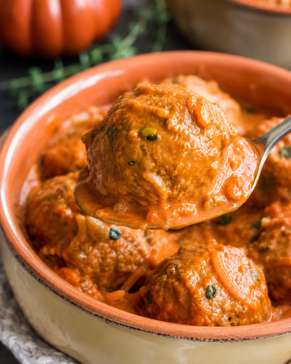 Spoon lifting a pumpkin turkey meatball from creamy harvest tomato sauce